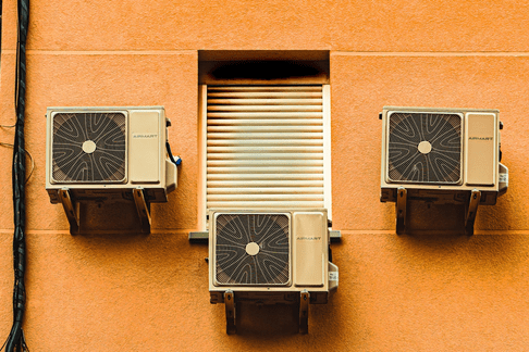 A trio of outdoor AC units on a yellow wall