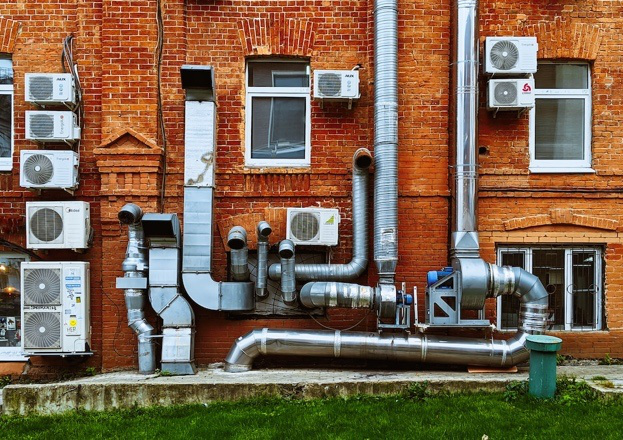 Pipes of an HVAC system against a red brick wall